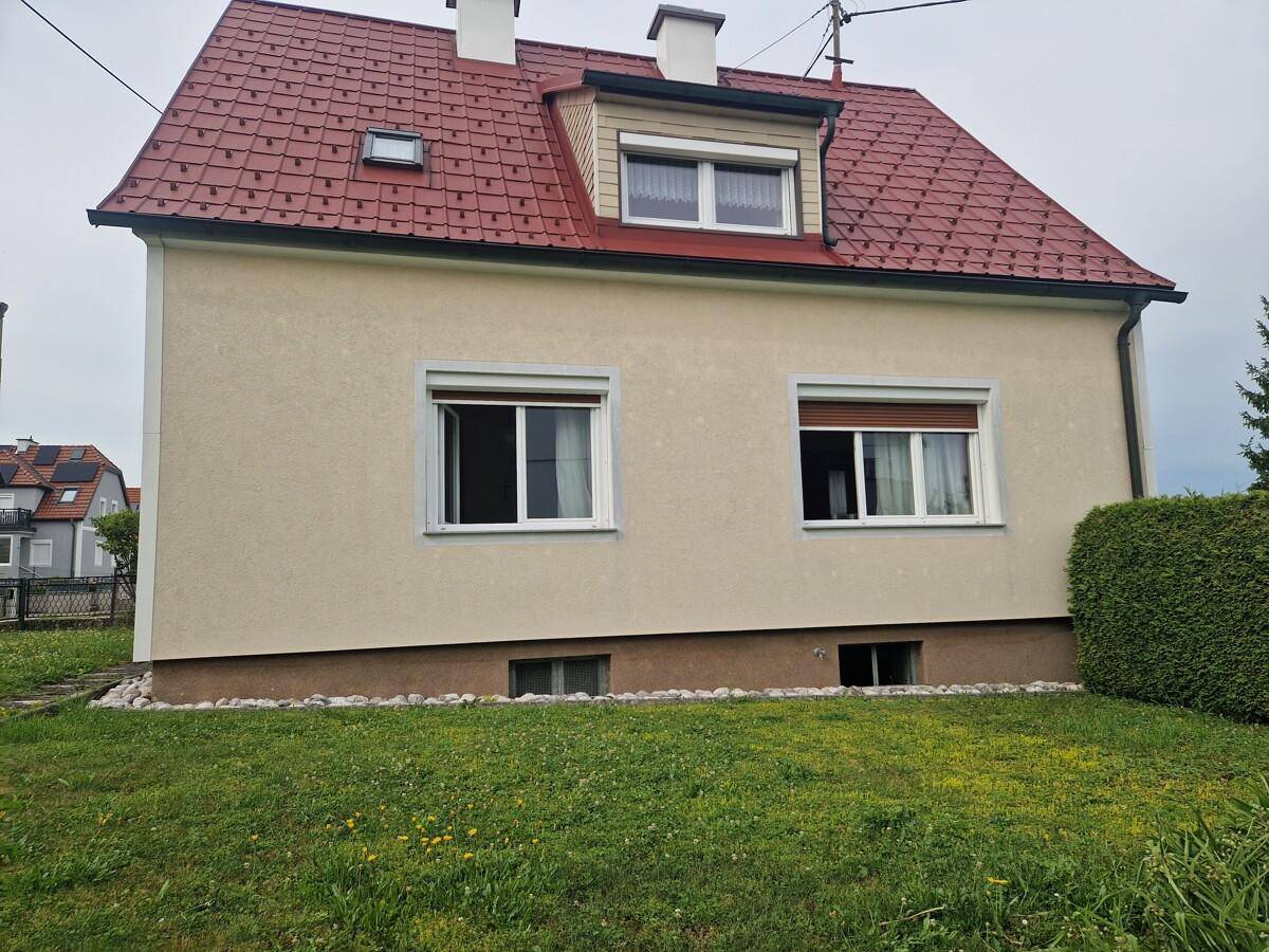 Seitenansicht des Hauses mit rotem Dach, beiger Fassade und Rollläden an den Fenstern.