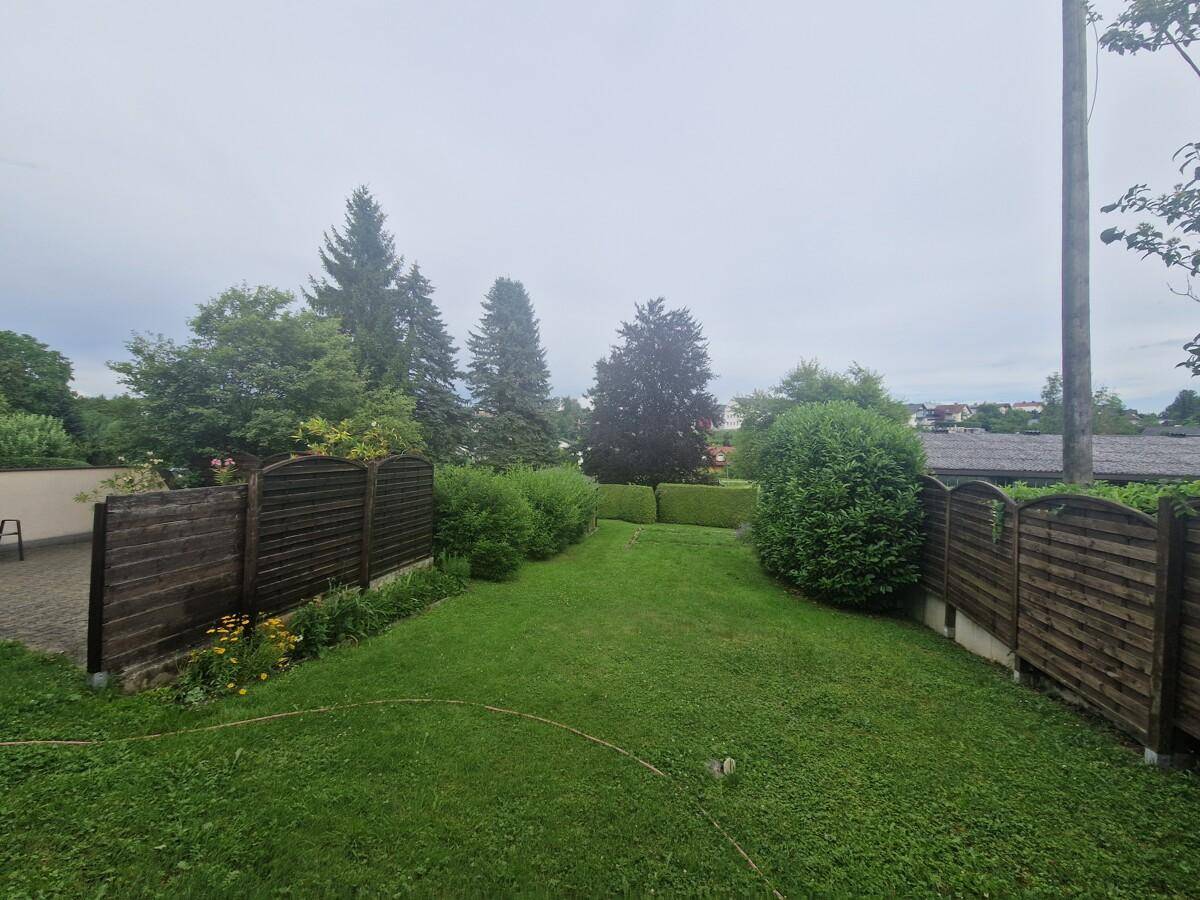 Großer, gepflegter Gartenbereich mit Rasenfläche und Holzzäunen, umgeben von Bäumen.