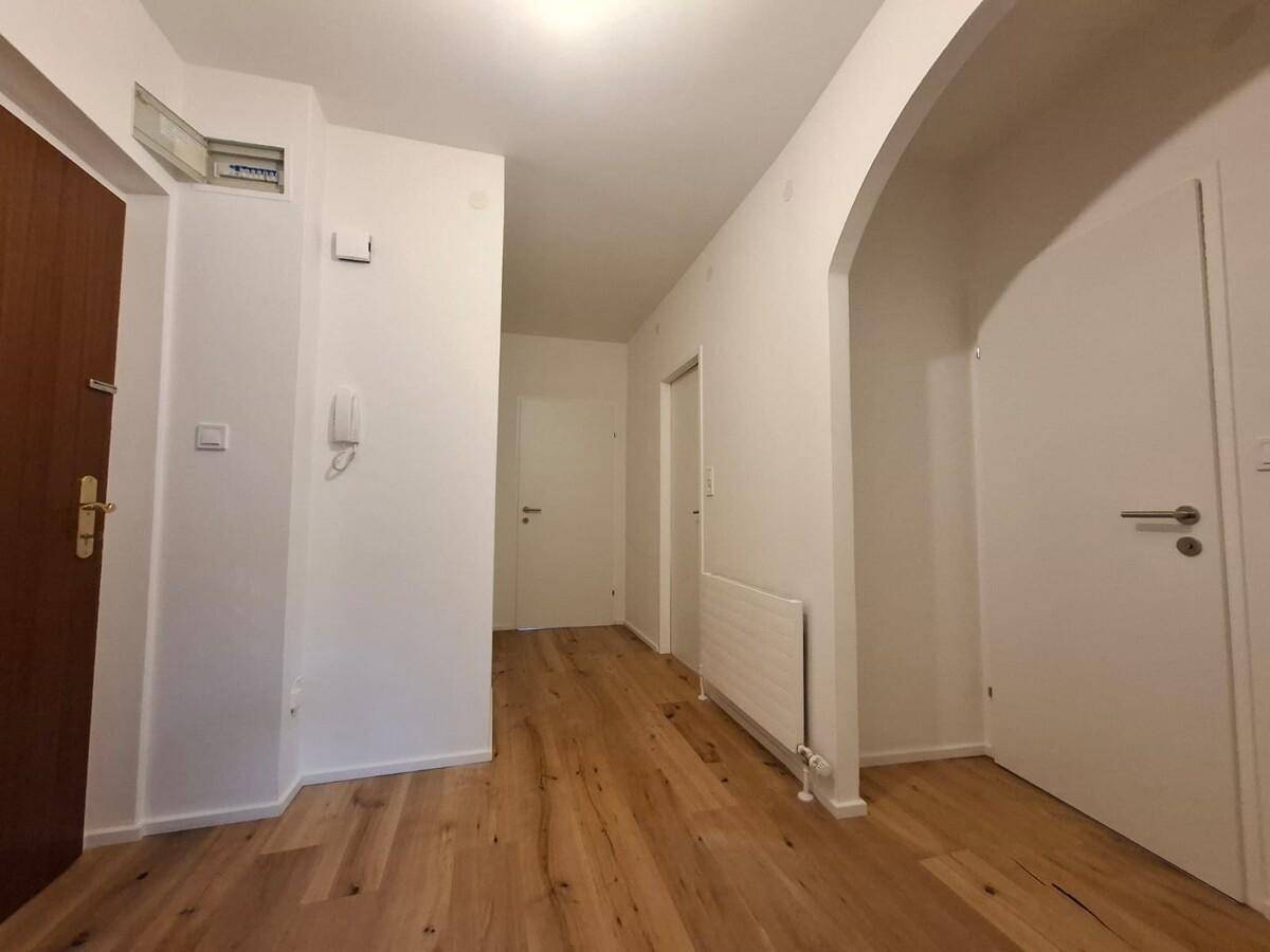 Geräumiger Flur mit Holzboden, Heizkörper und Zugang zu verschiedenen Zimmern.