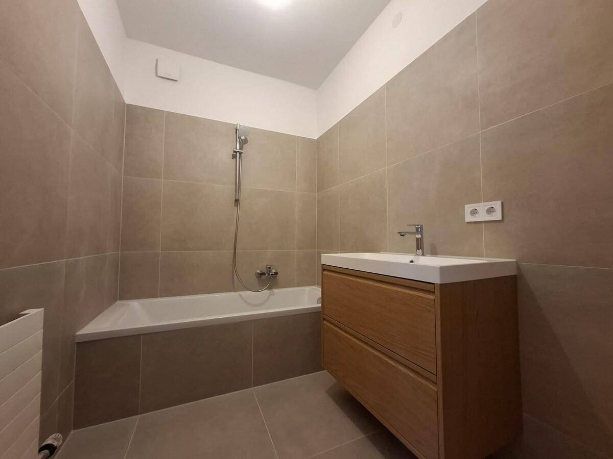 Modernes Badezimmer mit Badewanne, Einzelwaschbecken und beigefarbenen Fliesen.