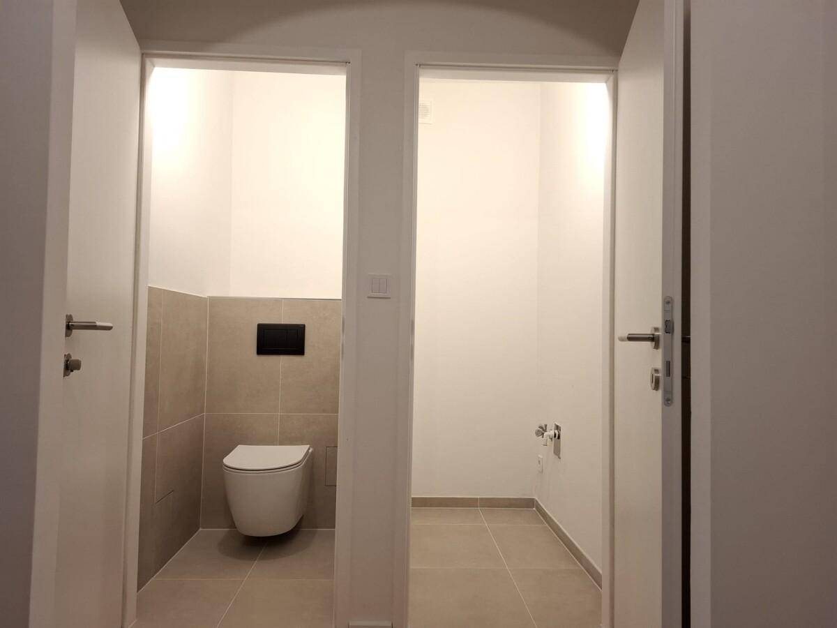 Separates WC mit Wandtoilette und angrenzendem Raum, möglicherweise für eine Dusche.