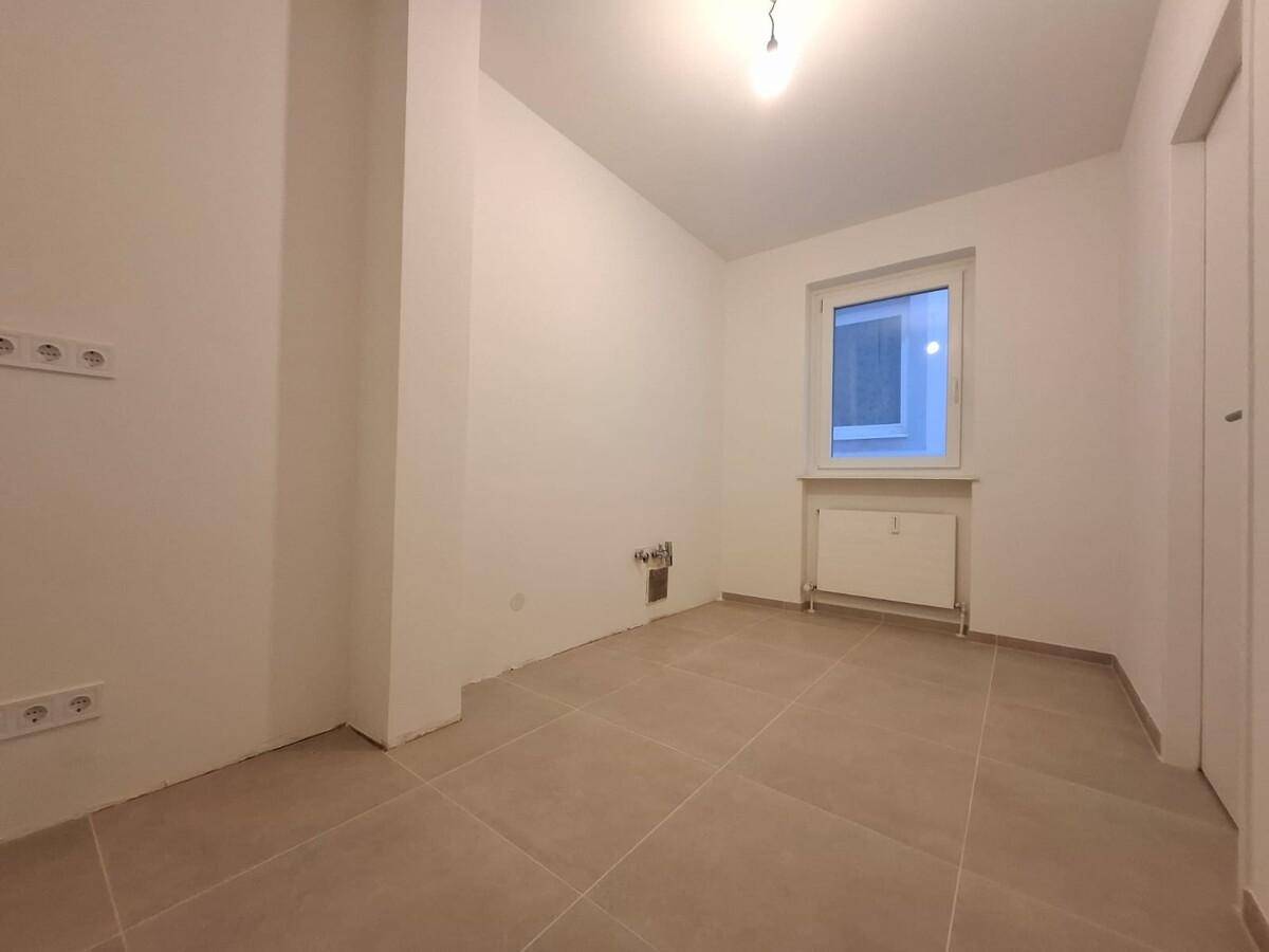 Leerer Küchenbereich mit Fliesenboden und Fenster, bereit für die Installation einer neuen Küche.