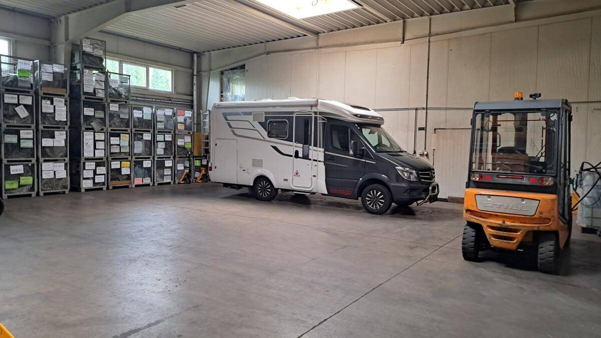 Großer Lager- oder Werkstattbereich mit Wohnmobil, Gabelstapler und hohen Regalen voller eingelagerter Gegenstände.