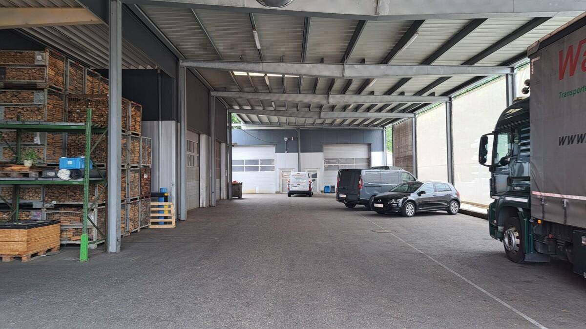 Überdachter Außenbereich oder offene Lagerhalle mit geparkten Fahrzeugen und Regalen voller Waren.