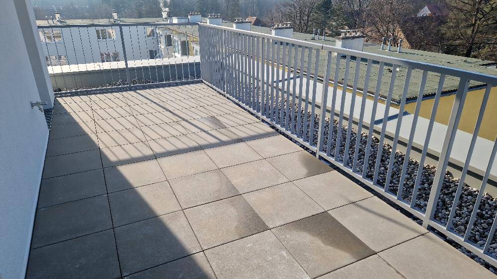 Heller Balkon mit Fliesenboden und Metallgeländer, bietet Blick auf die Umgebung.