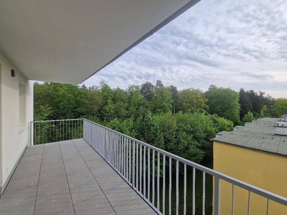 Balkon mit Fliesenboden und Blick auf grüne Bäume und ein angrenzendes Gebäude.