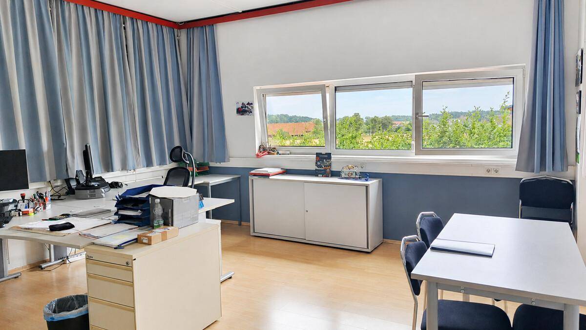 Büroraum mit Schreibtischen, Stühlen und einem großen Fenster, das einen weiten Blick ins Grüne bietet.