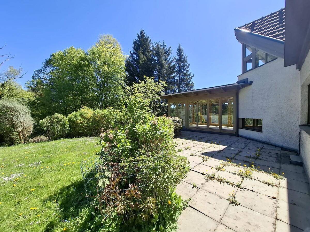 Gepflasterte Terrasse neben dem Haus, umgeben von üppigem Grün und Gartenbereich.