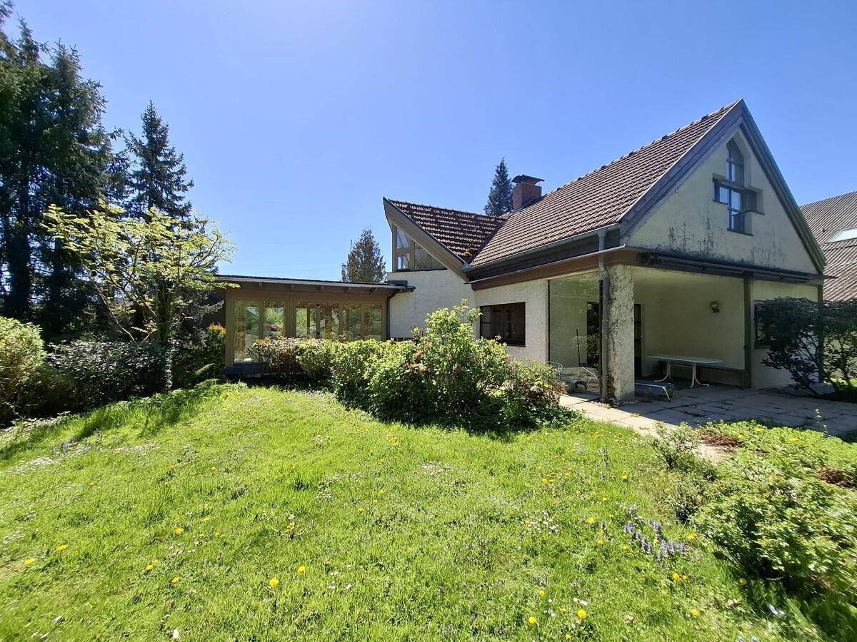 Hausansicht vom Garten mit einer Terrasse und einem angrenzenden verglasten Wintergarten.