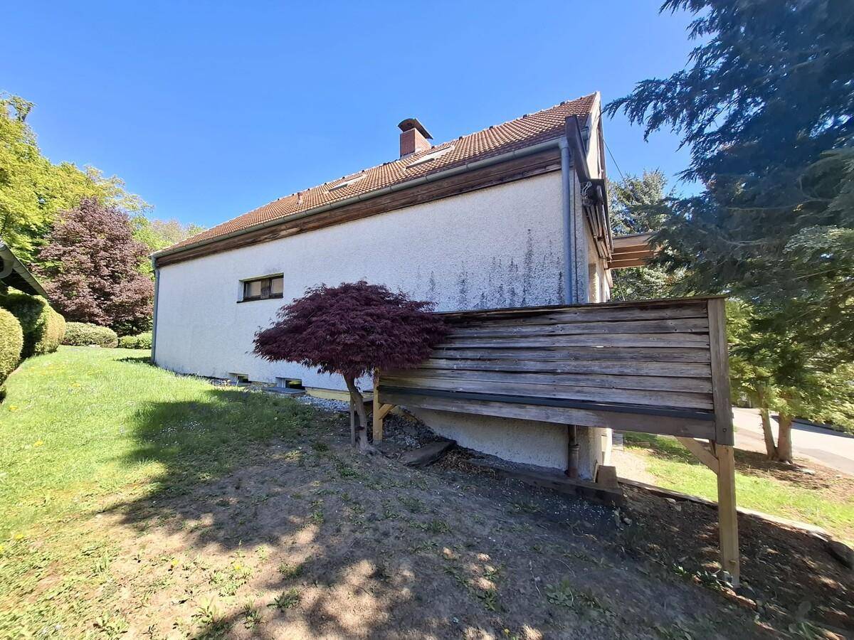 Seitenansicht des Hauses mit einer Holzverkleidung und einem kleinen Baum im Vorgarten.