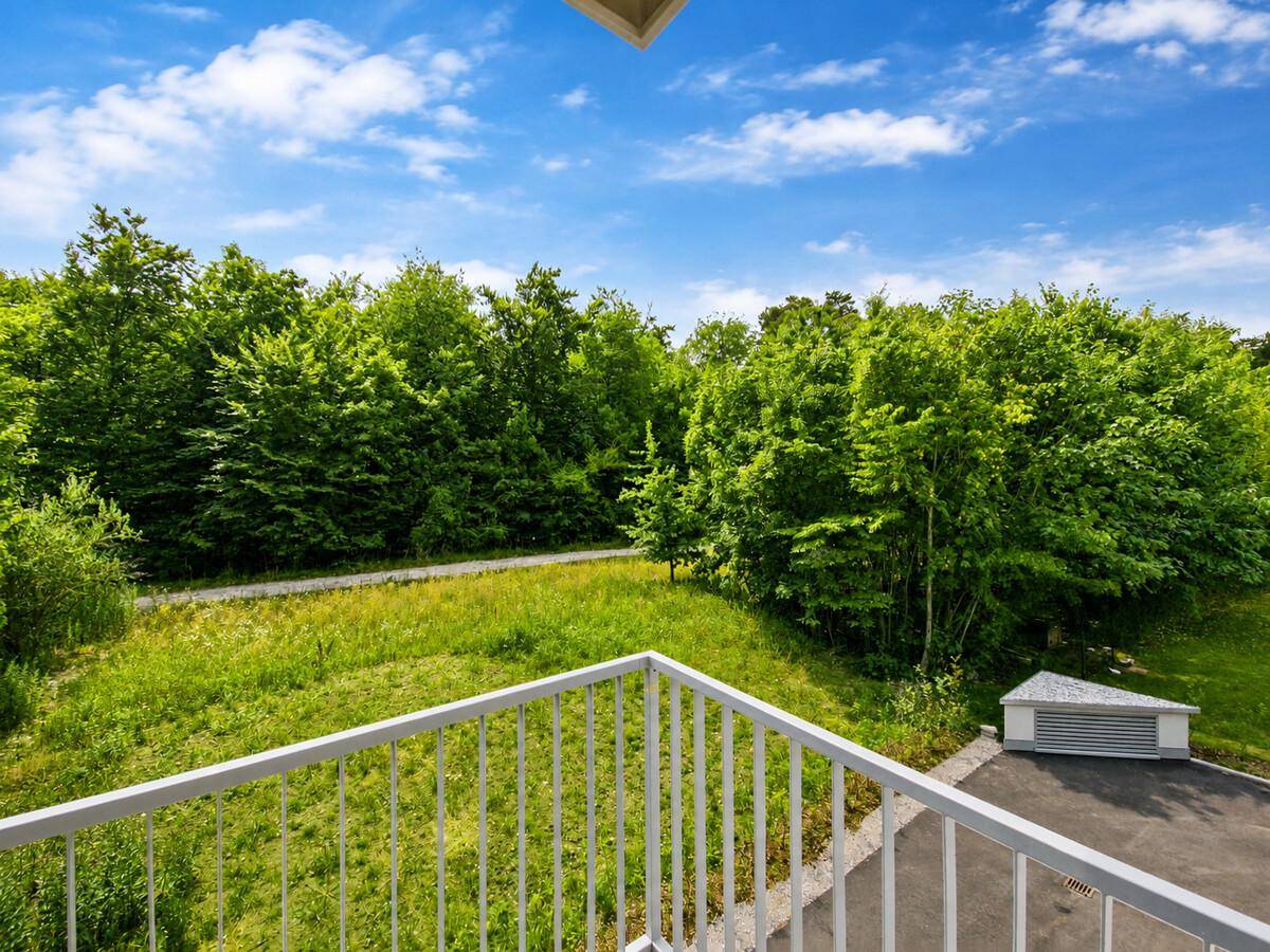 Balkon mit Blick auf eine weite grüne Waldlandschaft unter blauem Himmel.