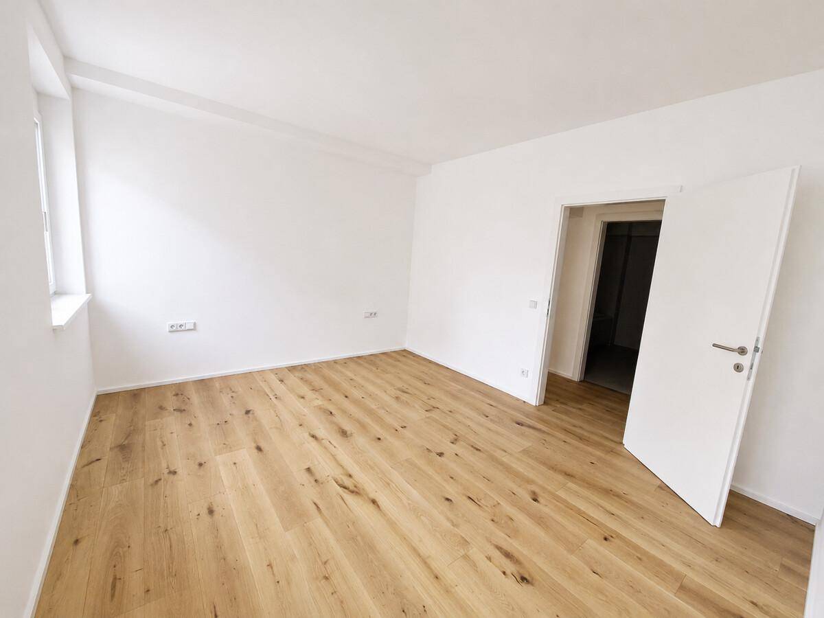 Geräumiger, heller Raum mit Holzboden und weiß gestrichenen Wänden.