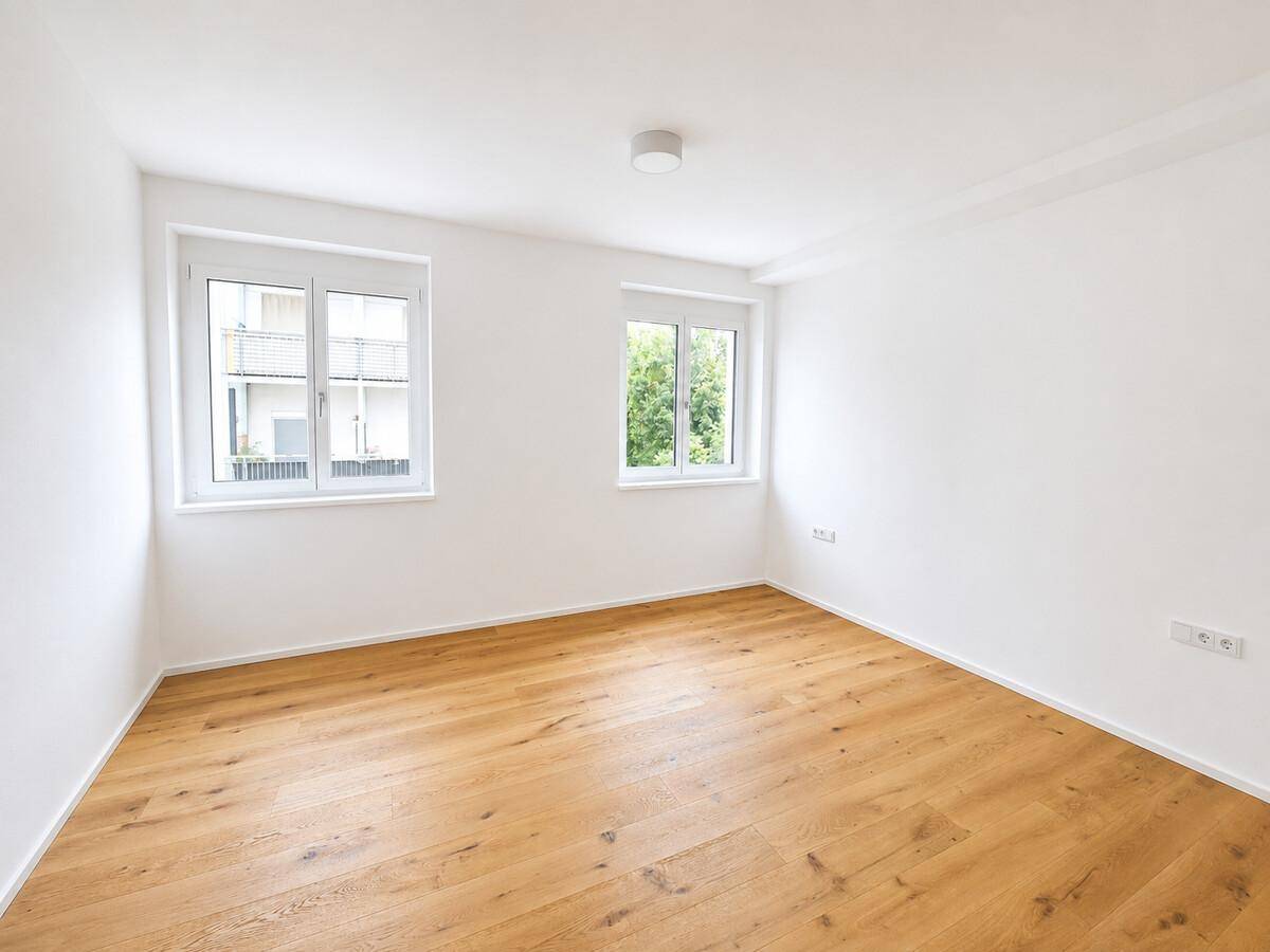 Heller, leerer Raum mit Holzboden und zwei Fenstern, bereit zur Einrichtung.