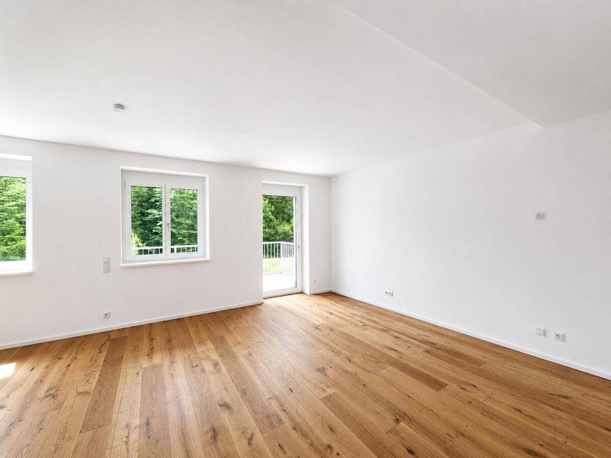 Heller Raum mit Holzboden, Fenstern und Zugang zu einem Balkon.