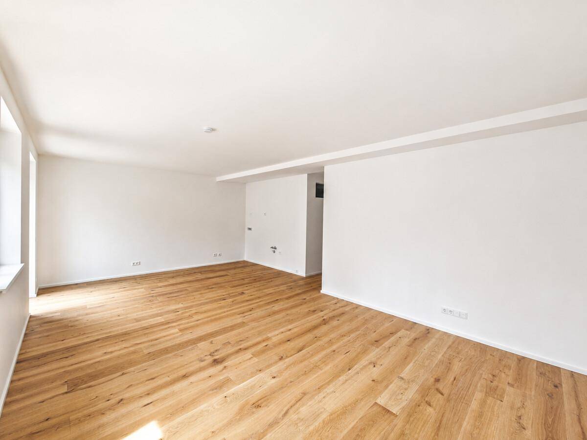Heller, geräumiger Raum mit Holzboden und weißen Wänden, ideal für offenes Wohnen.