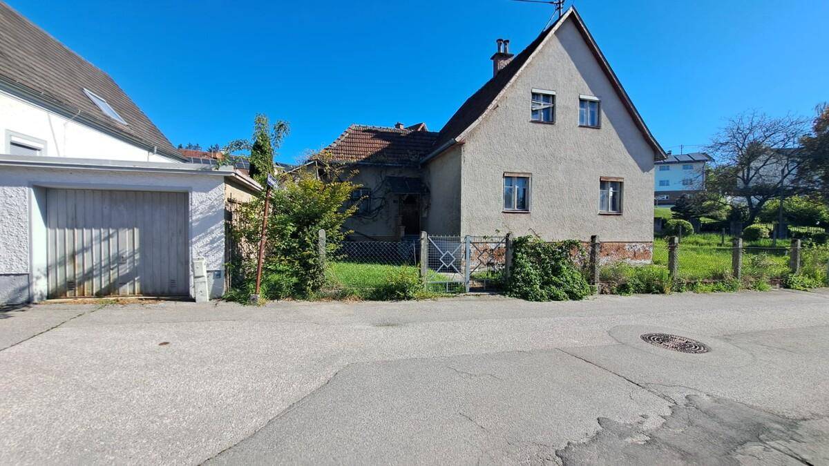 Ansicht eines Einfamilienhauses von der Straße mit angrenzender Garage und altem Zaun.