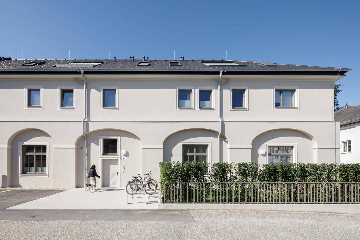 Modernes Gebäude mit heller Fassade, vielen Fenstern und gepflegter Hecke.