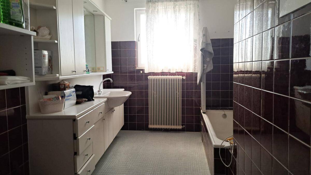Badezimmer mit Badewanne, Waschbecken und dunklen Fliesen.