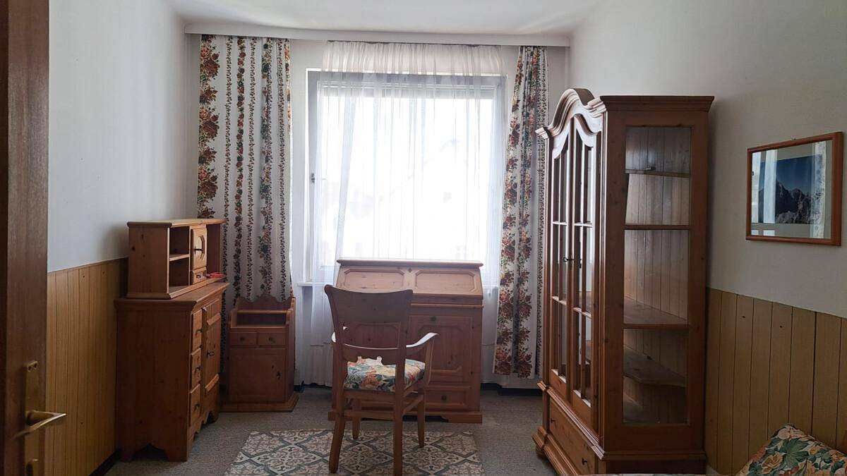 Arbeitszimmer mit Holzmöbeln, Schreibtisch und floralen Vorhängen.