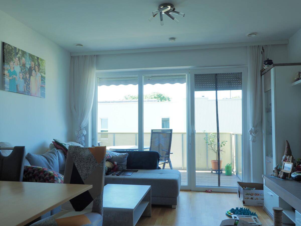 Helles Wohnzimmer mit Zugang zum Balkon, Sofa und Holzboden.