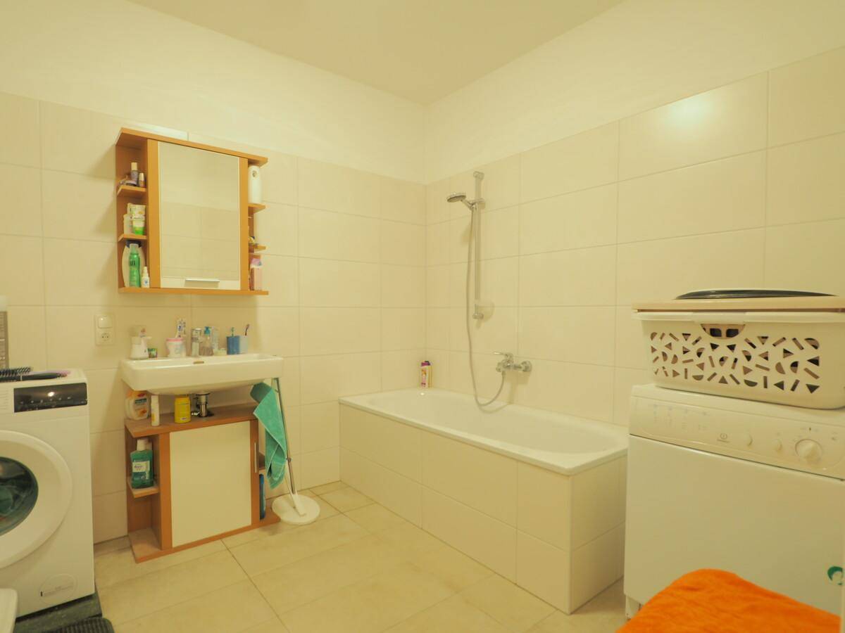 Helles Badezimmer mit Badewanne, Waschbecken und Waschmaschine, umgeben von hellen Fliesen.