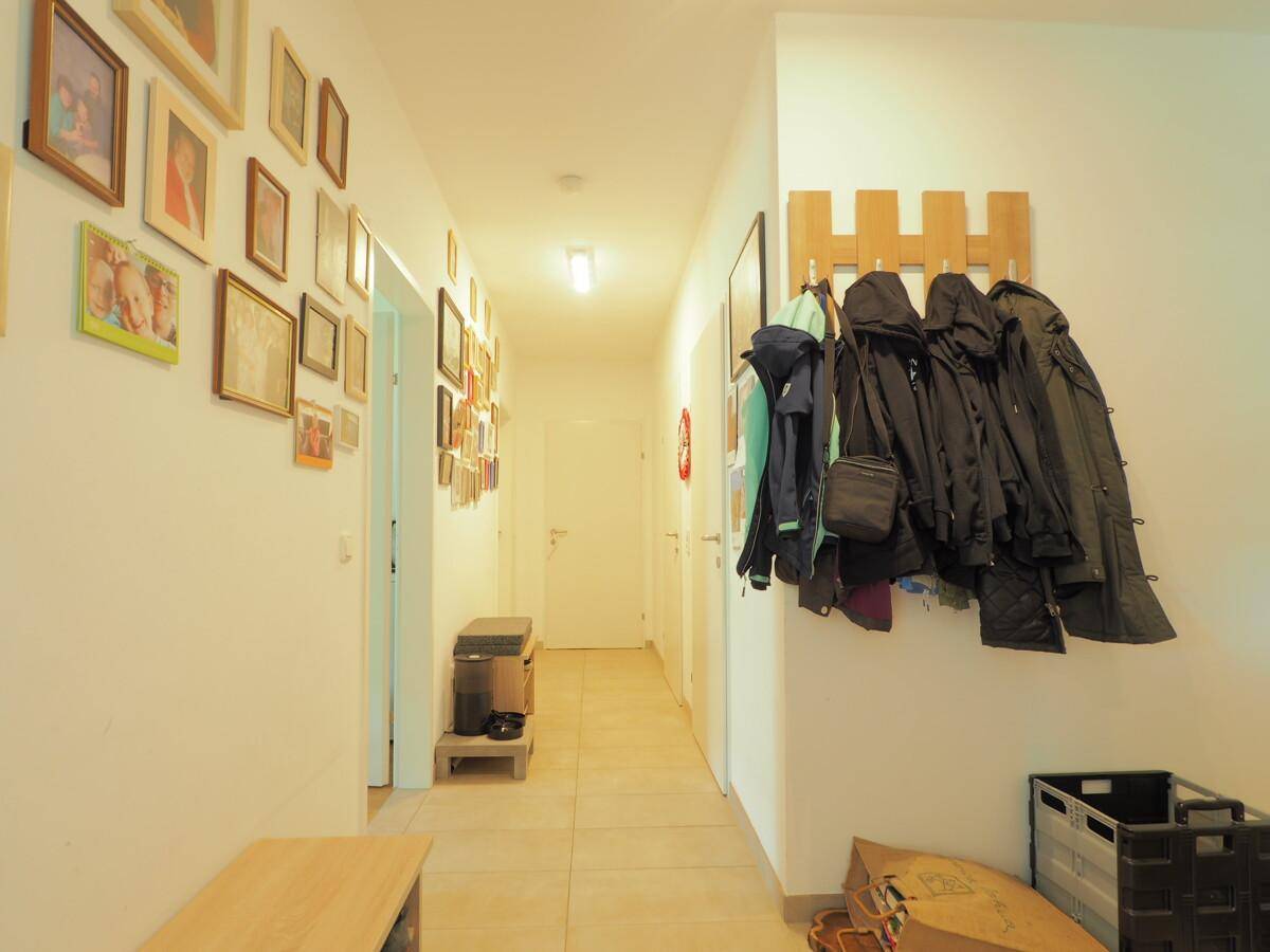 Langer Flur mit heller Fliesenboden, Garderobe und vielen gerahmten Bildern an der Wand.