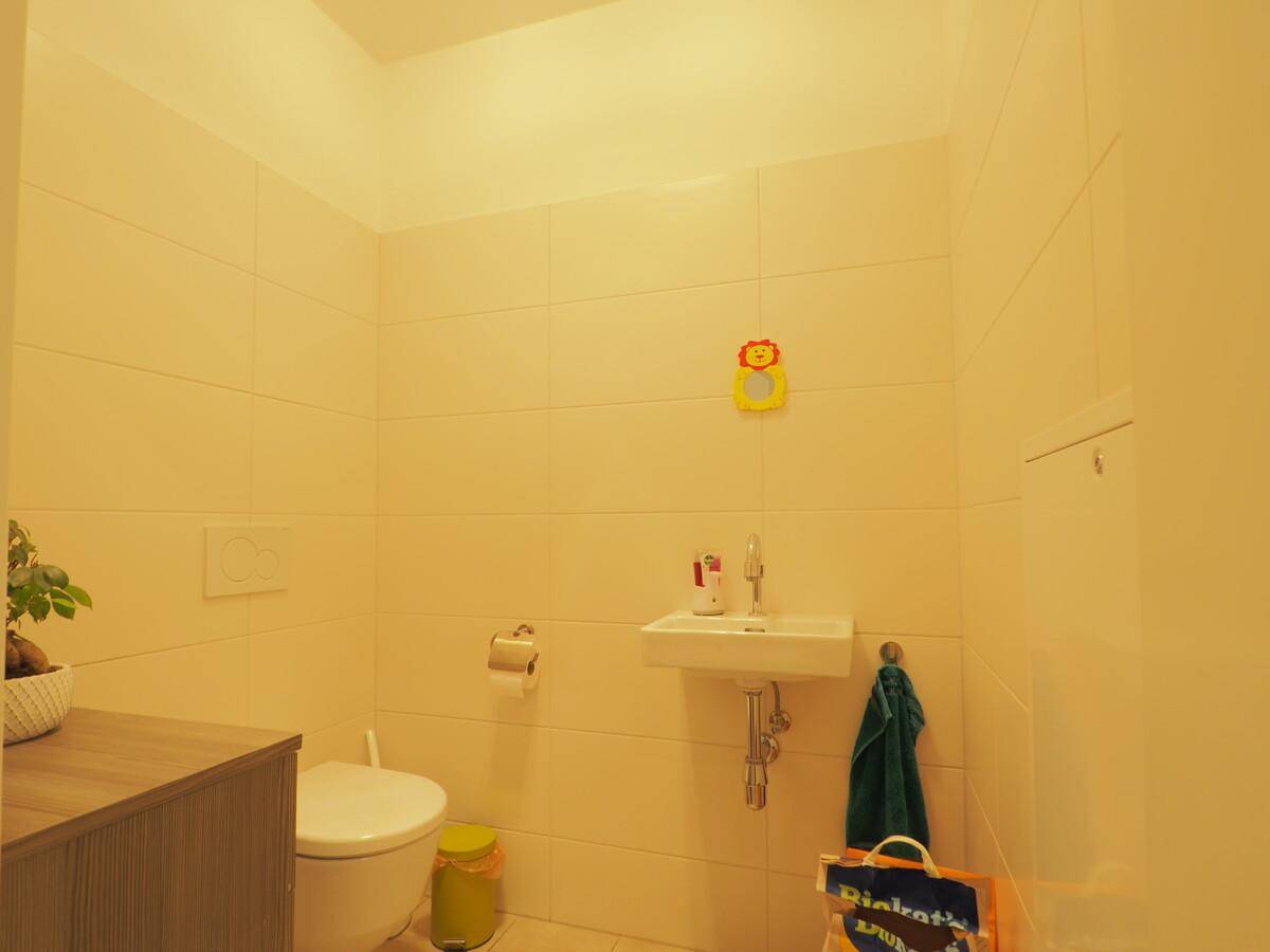 Kleines Gäste-WC mit Wand-WC, Waschbecken und hellen Fliesen an den Wänden.