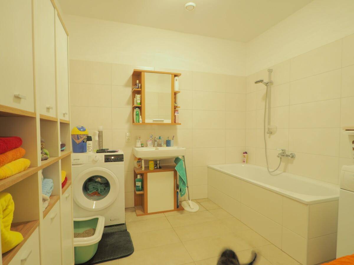 Badezimmer mit Badewanne, Waschbecken, Waschmaschine und hellen Fliesen.