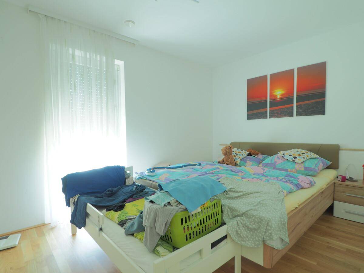 Schlafzimmer mit Doppelbett, Holzboden und Fenster mit viel Tageslicht.
