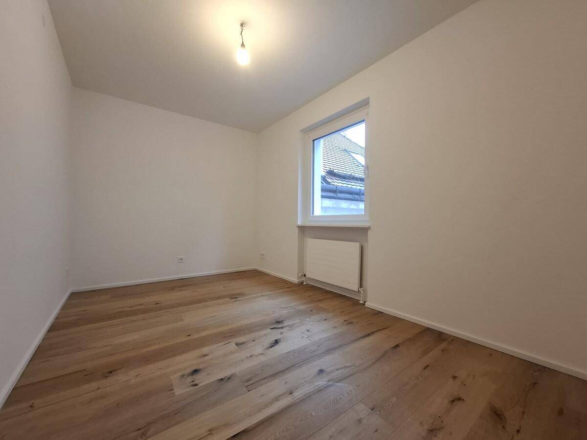 Leeres Schlafzimmer mit hellem Holzboden und einem Fenster mit Blick nach draußen.