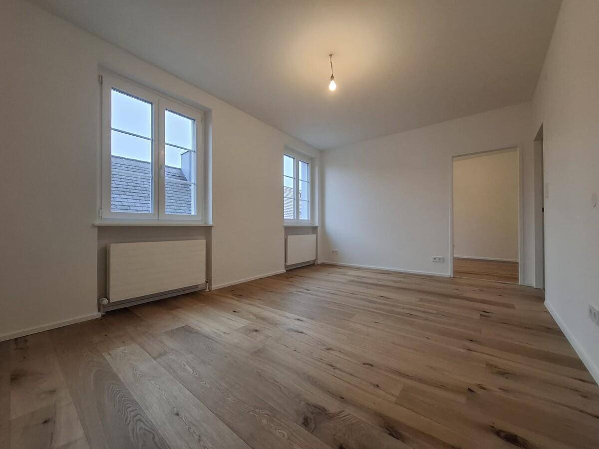 Geräumiges Wohnzimmer mit hellem Holzboden und Blick auf die Umgebung.