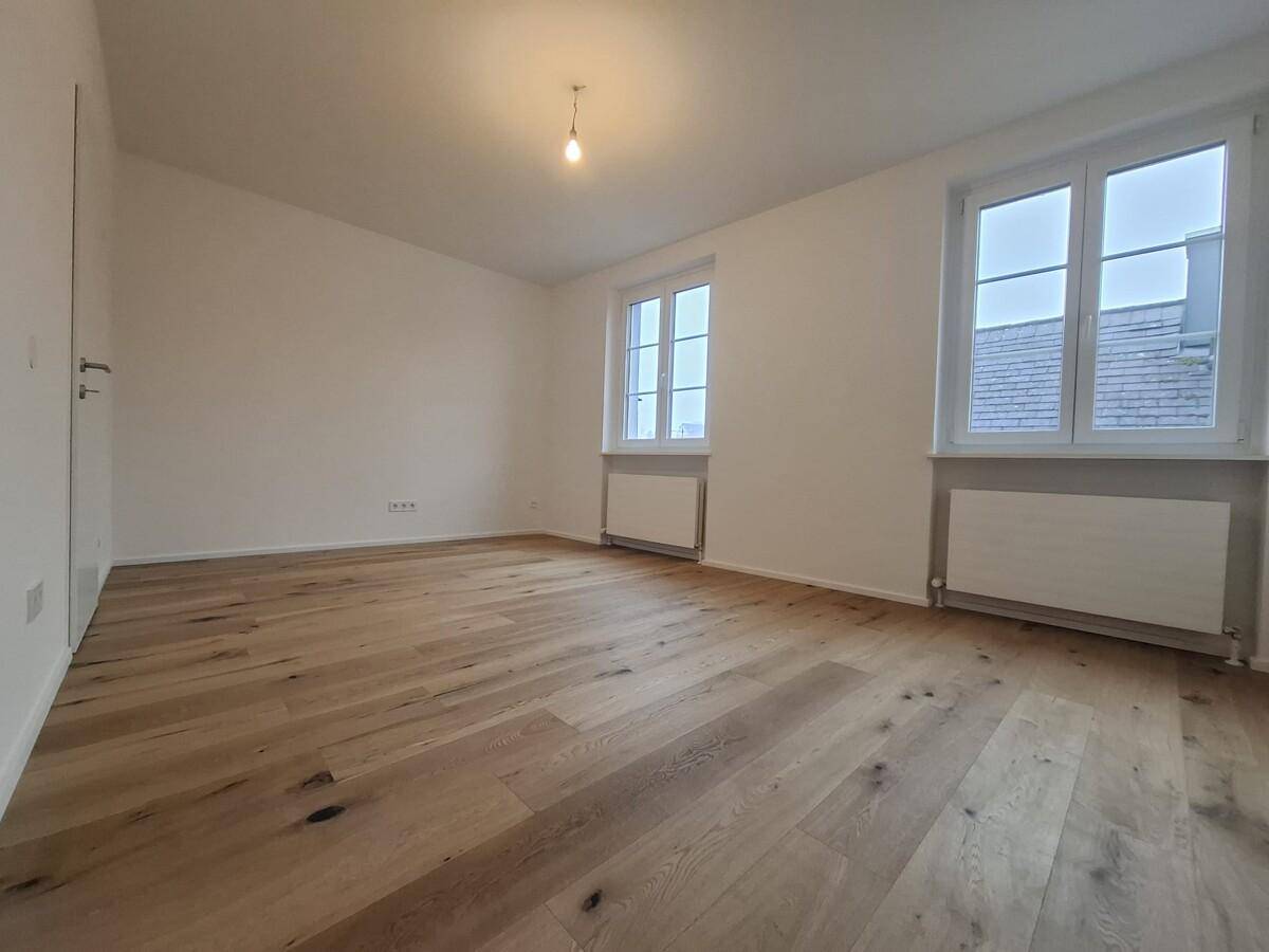 Helles, leeres Wohnzimmer mit neuem Holzboden und zwei großen Fenstern.
