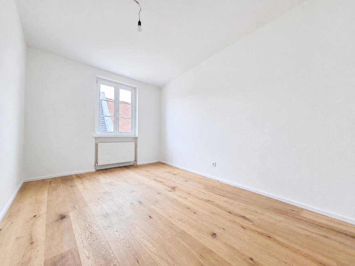 Helles, leeres Zimmer mit Holzboden und einem Fenster, bietet vielseitige Nutzungsmöglichkeiten.