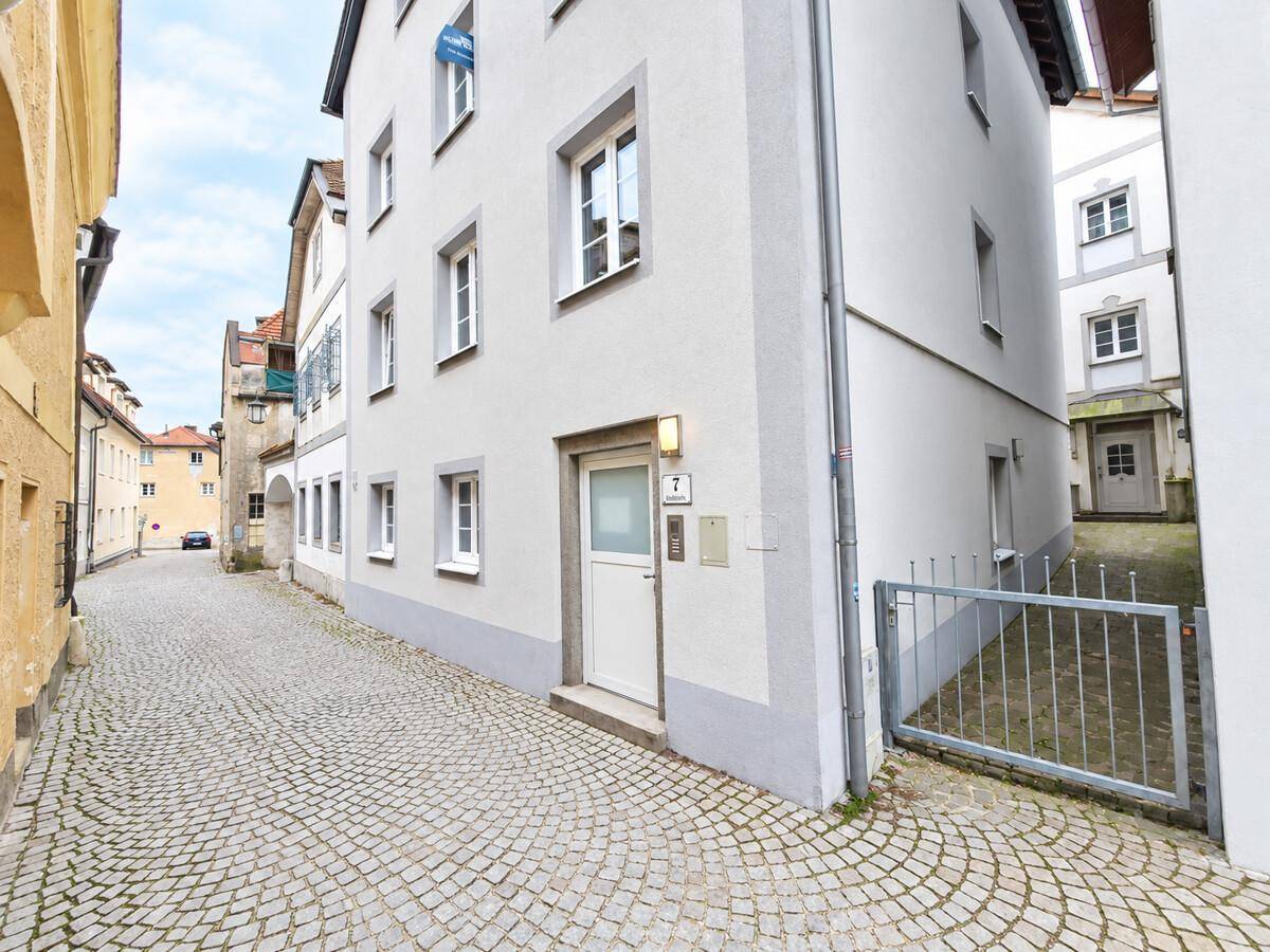 Gebäude in einer Kopfsteinpflastergasse mit Eingangstür und einem kleinen Zaunbereich.