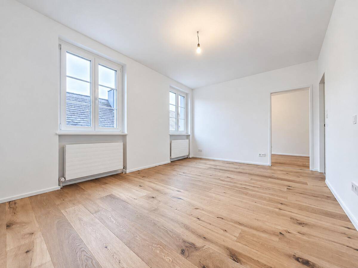 Geräumiges, helles Zimmer mit Holzboden und Zugang zu einem weiteren Raum, ideal für Wohnzwecke.