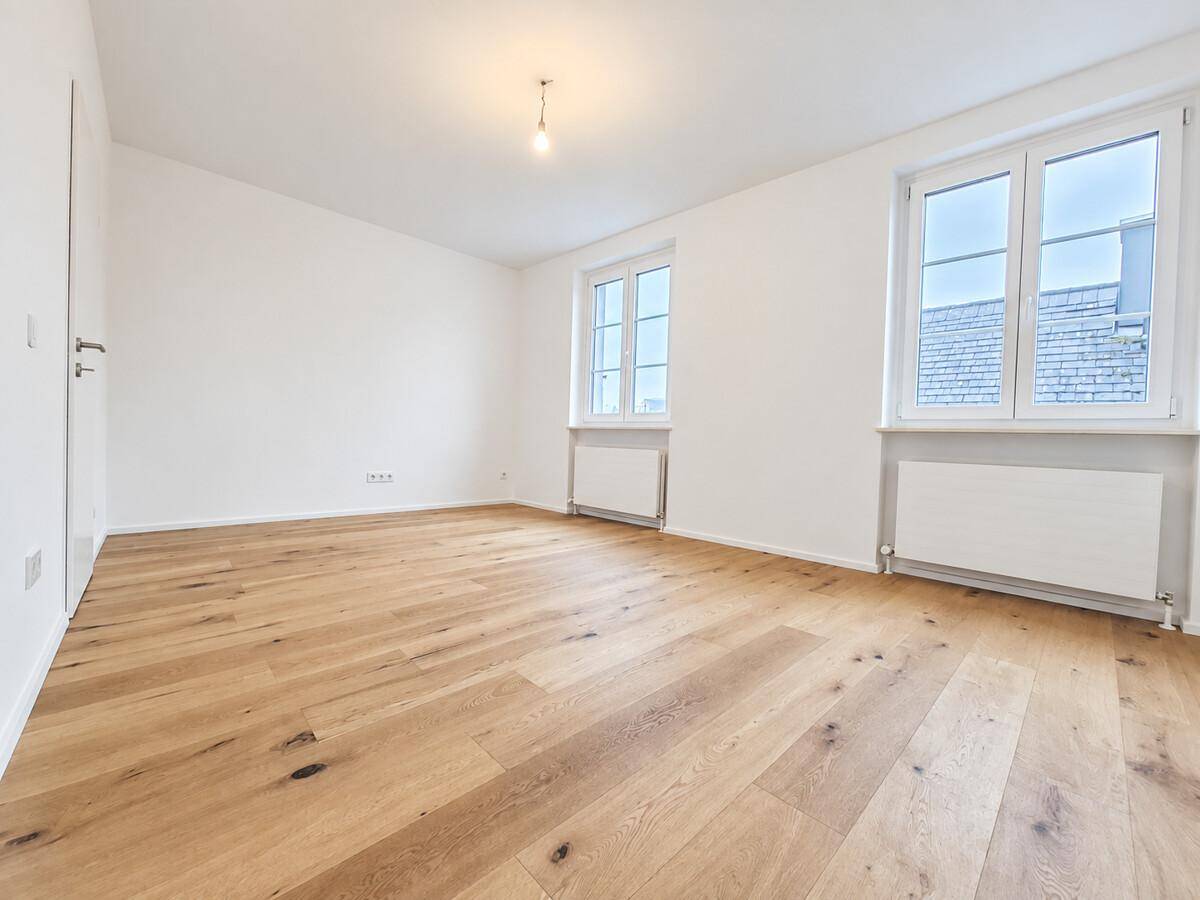 Helles, leeres Zimmer mit neuem Holzboden und zwei Fenstern, bereit zur individuellen Gestaltung.