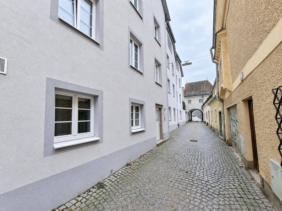 Historische Gasse mit Kopfsteinpflaster und traditionellen Gebäudefassaden unter bewölktem Himmel.