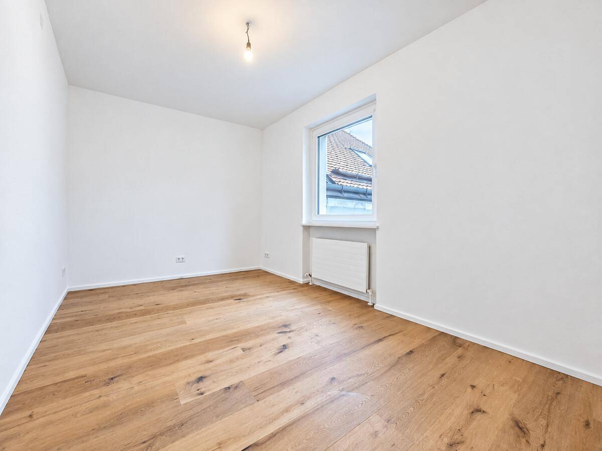 Helles, leeres Schlafzimmer mit Holzboden und einem Fenster, bereit zur Einrichtung.