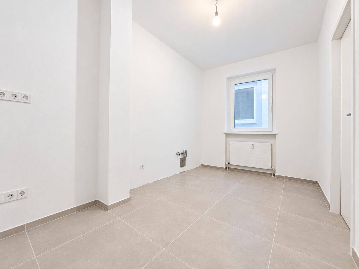 Leerer Raum mit Fliesenboden und Fenster, vorbereitet für eine Kücheninstallation oder als Abstellraum.