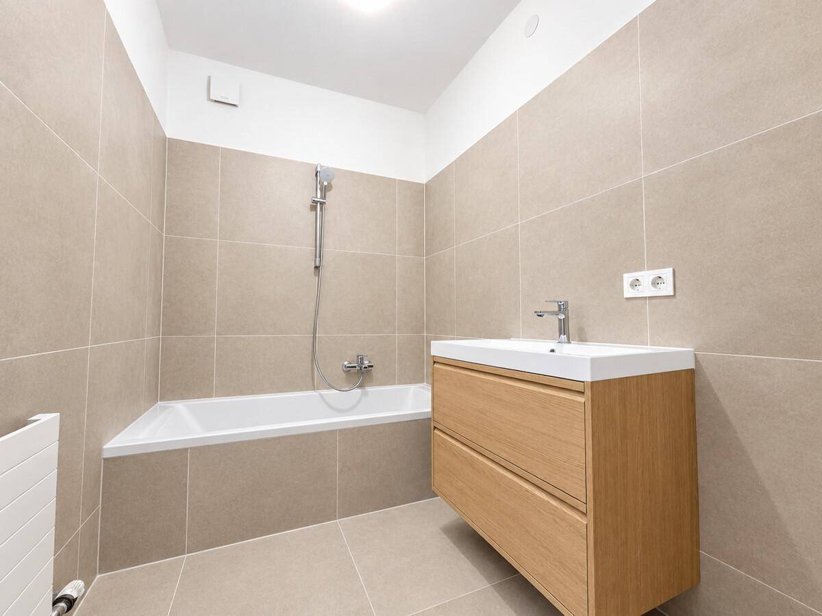 Modernes Badezimmer mit beigefarbenen Fliesen, Badewanne und Waschtisch mit Holzunterschrank.