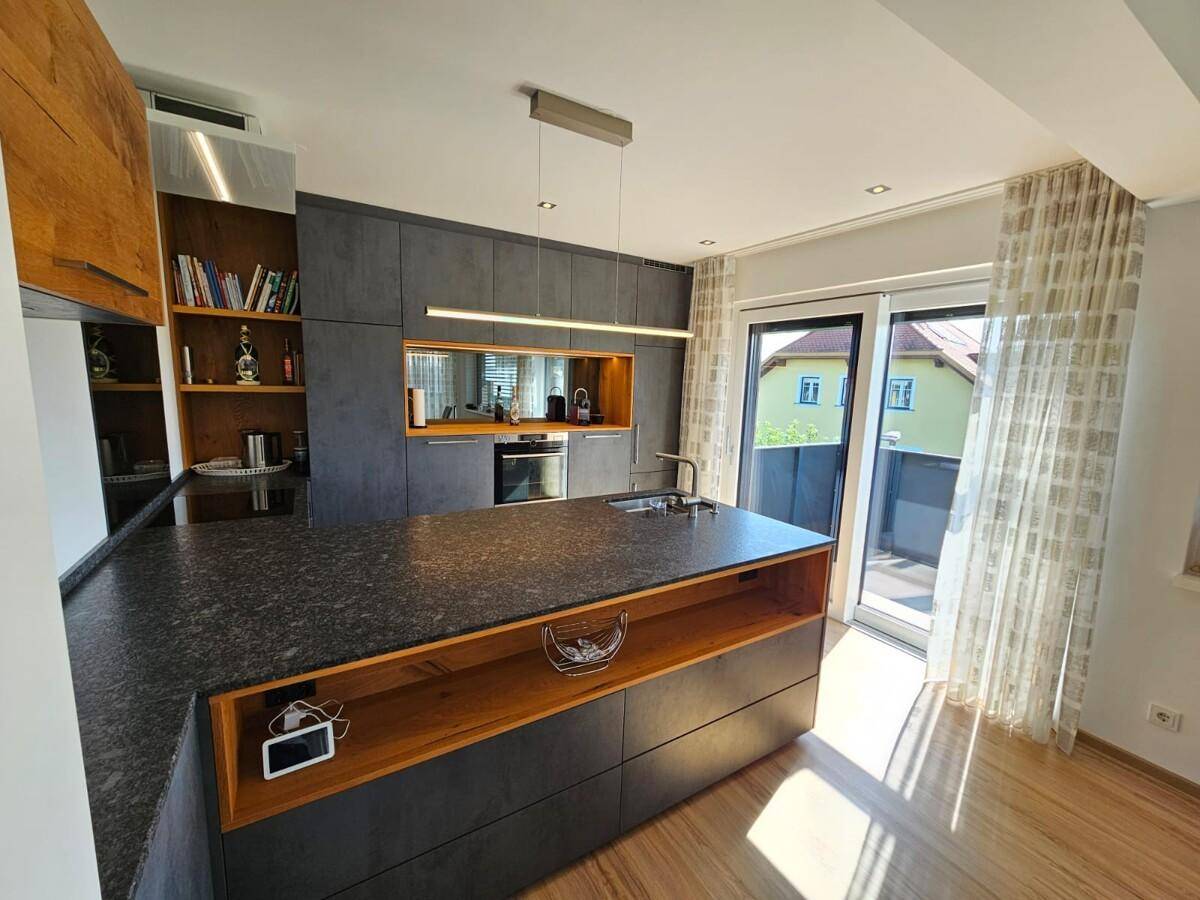 Moderne Küche mit großer Kochinsel, dunklen Arbeitsplatten und direktem Zugang zur Terrasse.