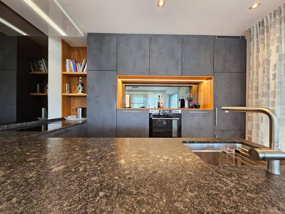 Moderne Küche mit dunklen Granitarbeitsplatten, integriertem Backofen und stilvollen Holzregalen.