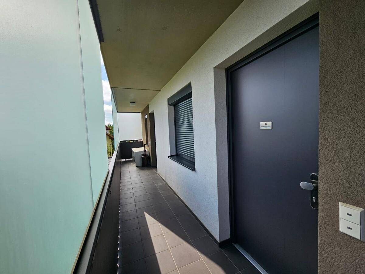 Langer Balkon mit Fliesenboden, dunkler Tür und Blick auf die Umgebung.