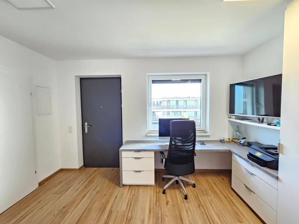 Funktionales Arbeitszimmer mit Schreibtisch, Bürostuhl und Blick aus dem Fenster.