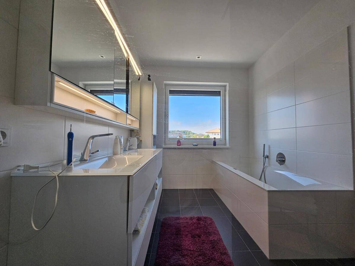 Modernes Badezimmer mit Doppelwaschbecken, Badewanne und Fenster für Tageslicht.