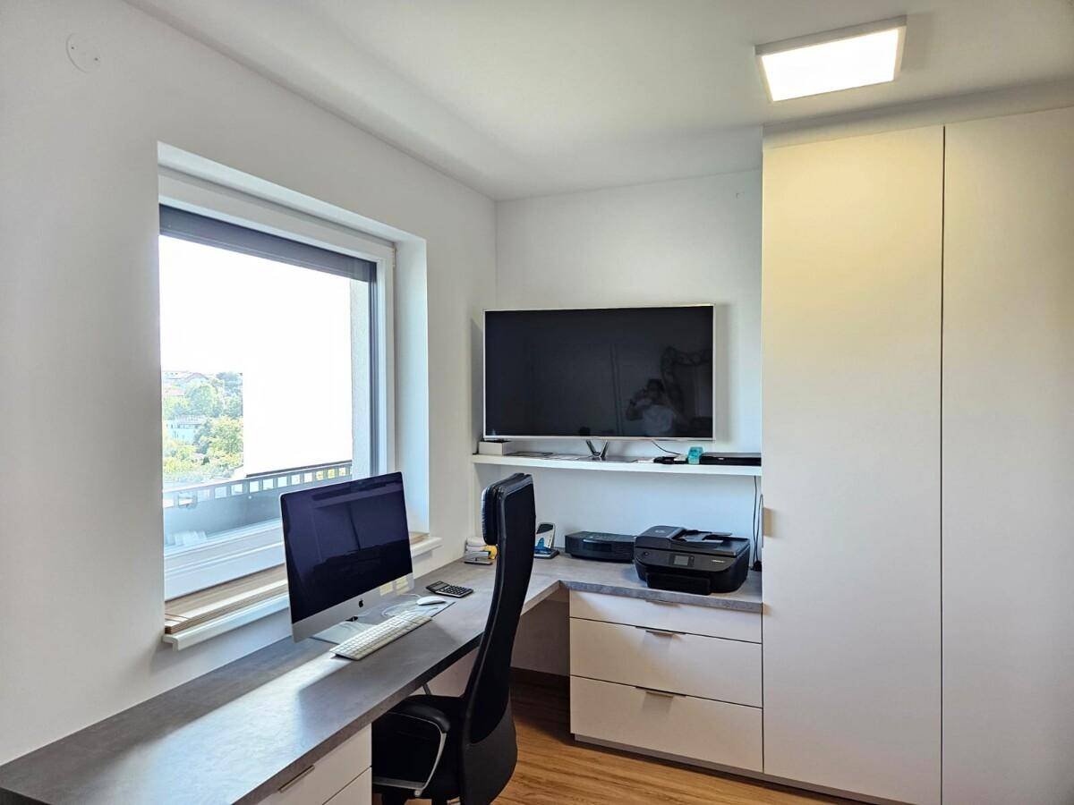 Helles Arbeitszimmer mit Schreibtisch, Computer und Fenster mit Ausblick.