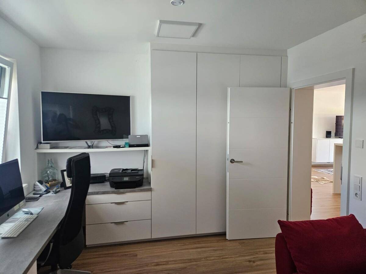 Arbeitszimmer mit integrierten Schränken, Schreibtisch und Fernseher an der Wand.