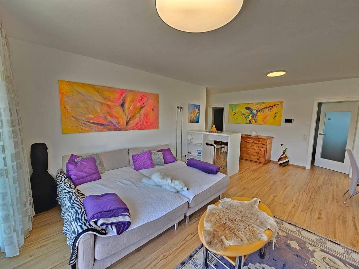 Gemütliches Wohnzimmer mit Sofa, farbenfrohen Kunstwerken und hellem Laminatboden.