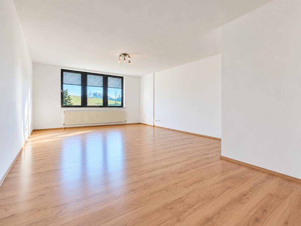 Helles Wohnzimmer mit Laminatboden, großem Fenster und Blick ins Grüne.