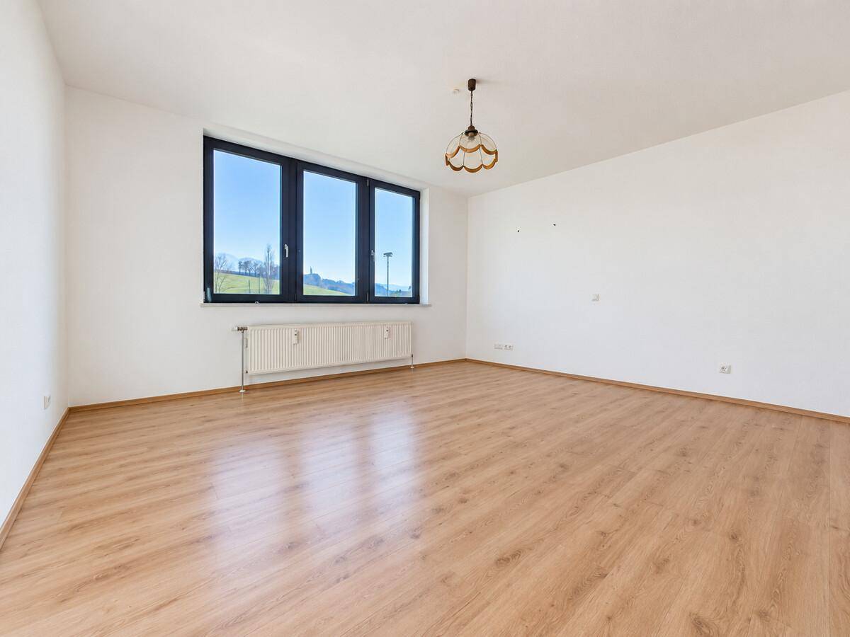 Leeres Schlafzimmer mit Laminatboden, großem Fenster und weitem Blick.
